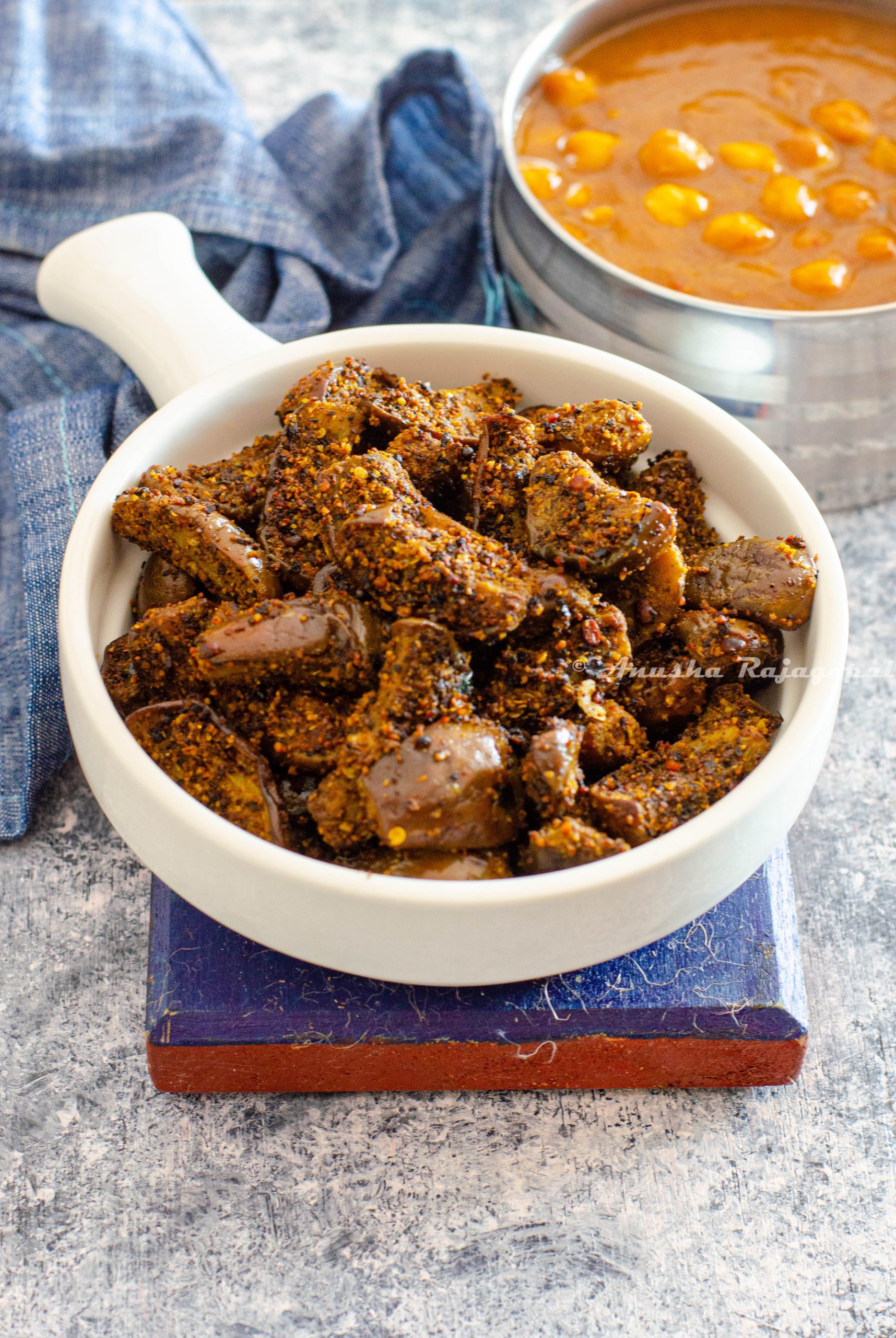 kathrikai podi curry- brinjal stir fry made with fresh spice powder served in a white shallow handled bowl placed on a blue coaster