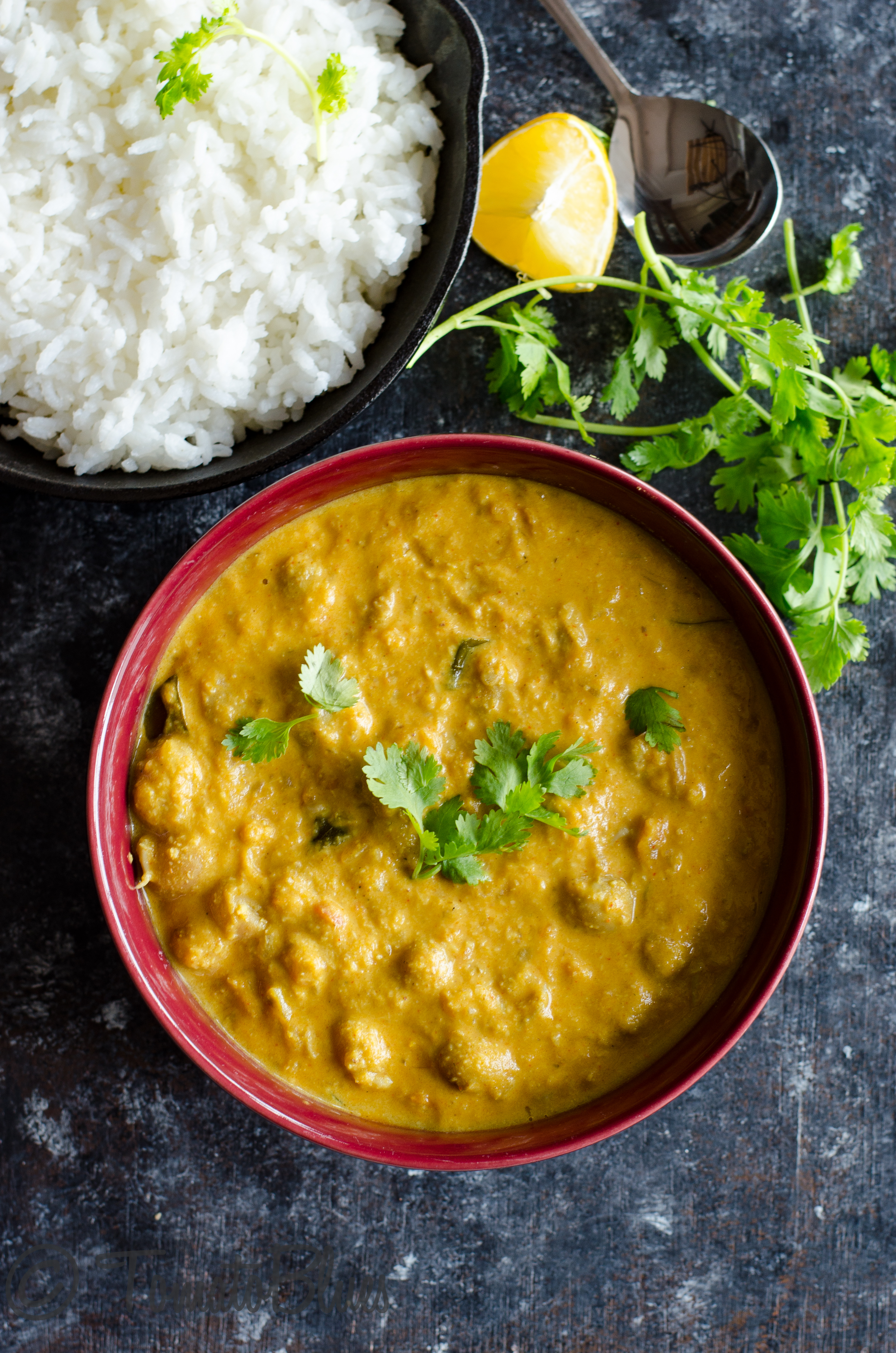 cranberry beans kurma served in a black bowl with lemon wedges and rice