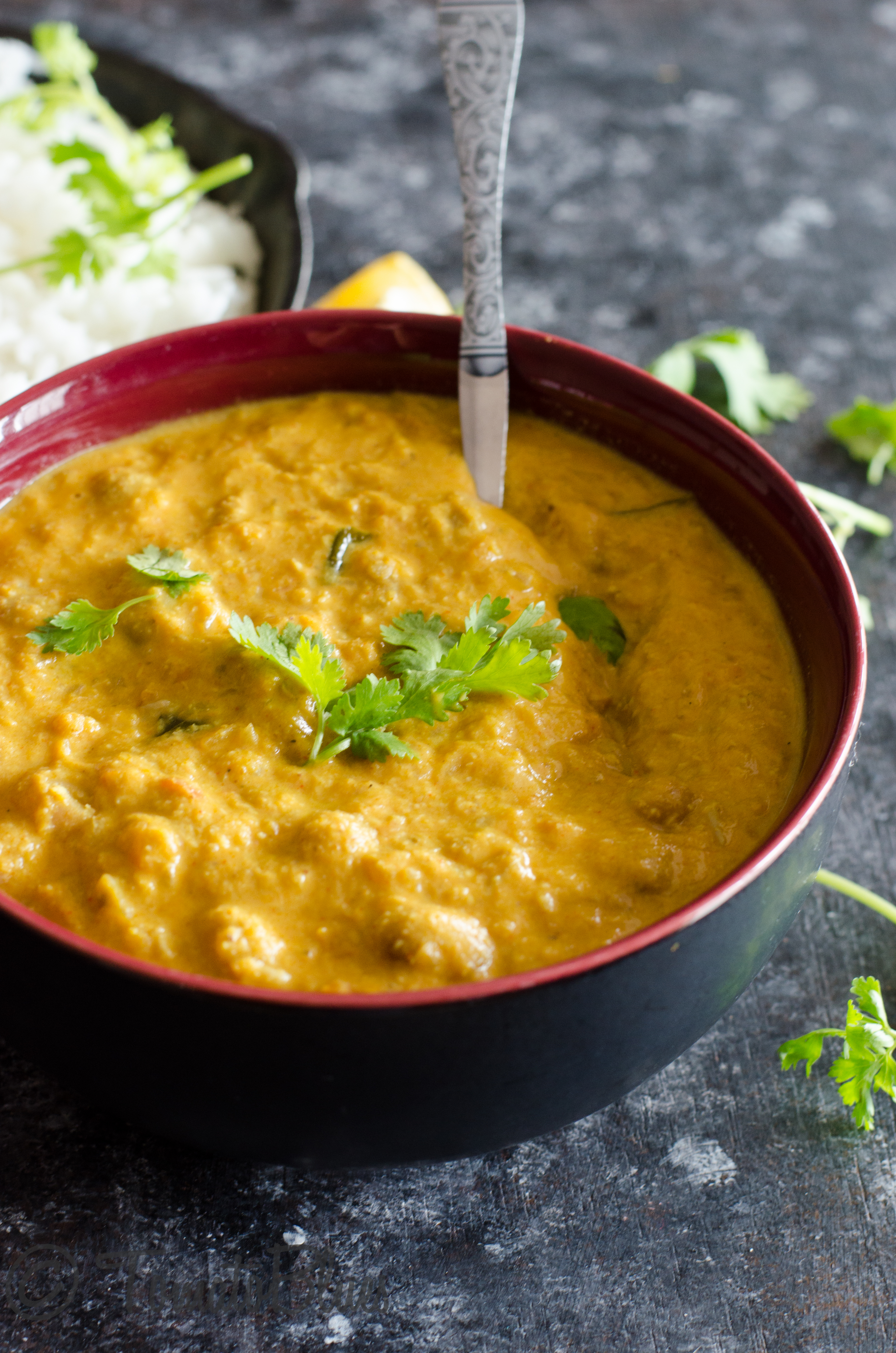 creamy cranberry beans kurma served in a black bowl with a spoon in it