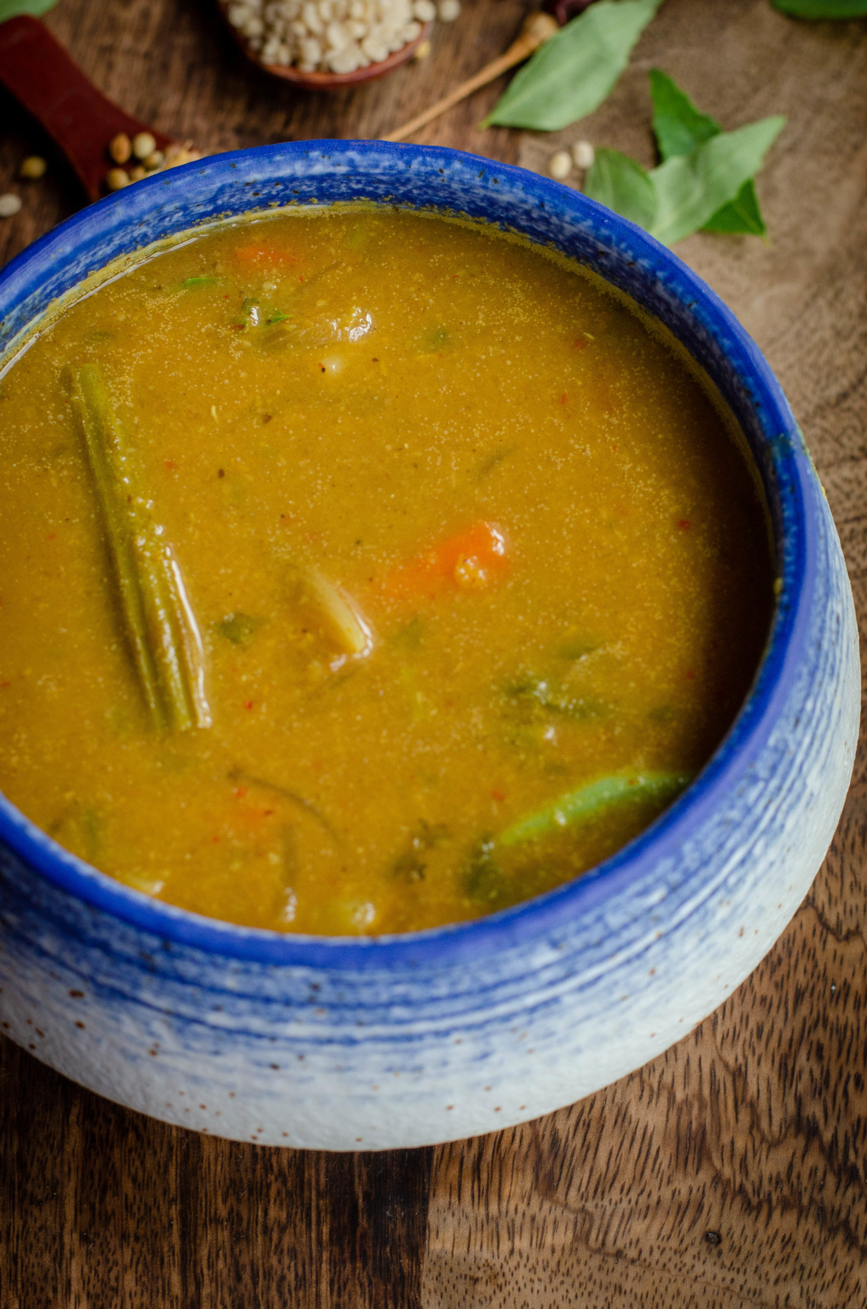 varutharacha kerala sambar served in a white bowl with blue rim on a wooden board with spices scattered around