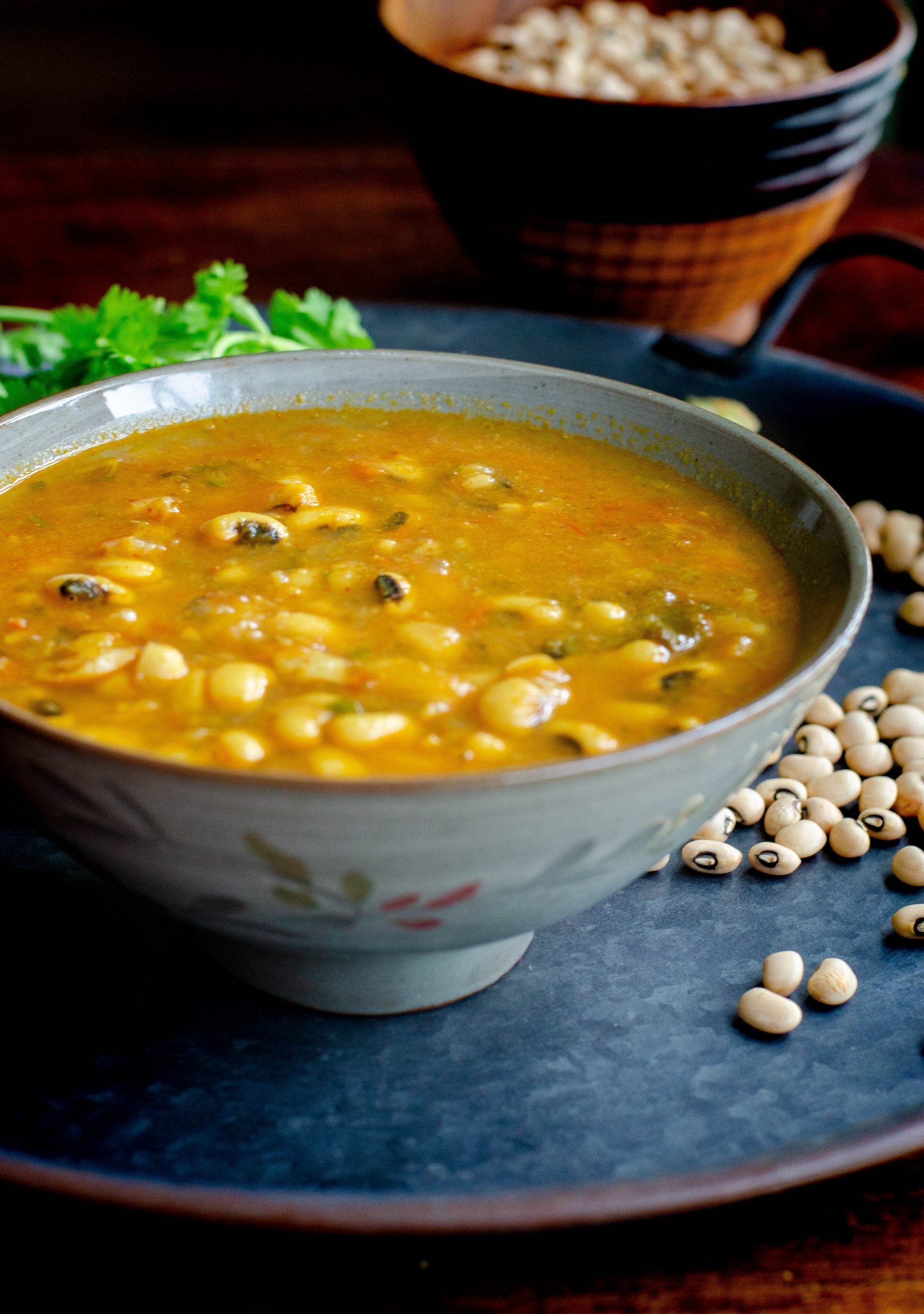 Black eyed peas curry served in a grey bowl placed on a blackish gray tray with scattered black eyed peas and cilantro at the background