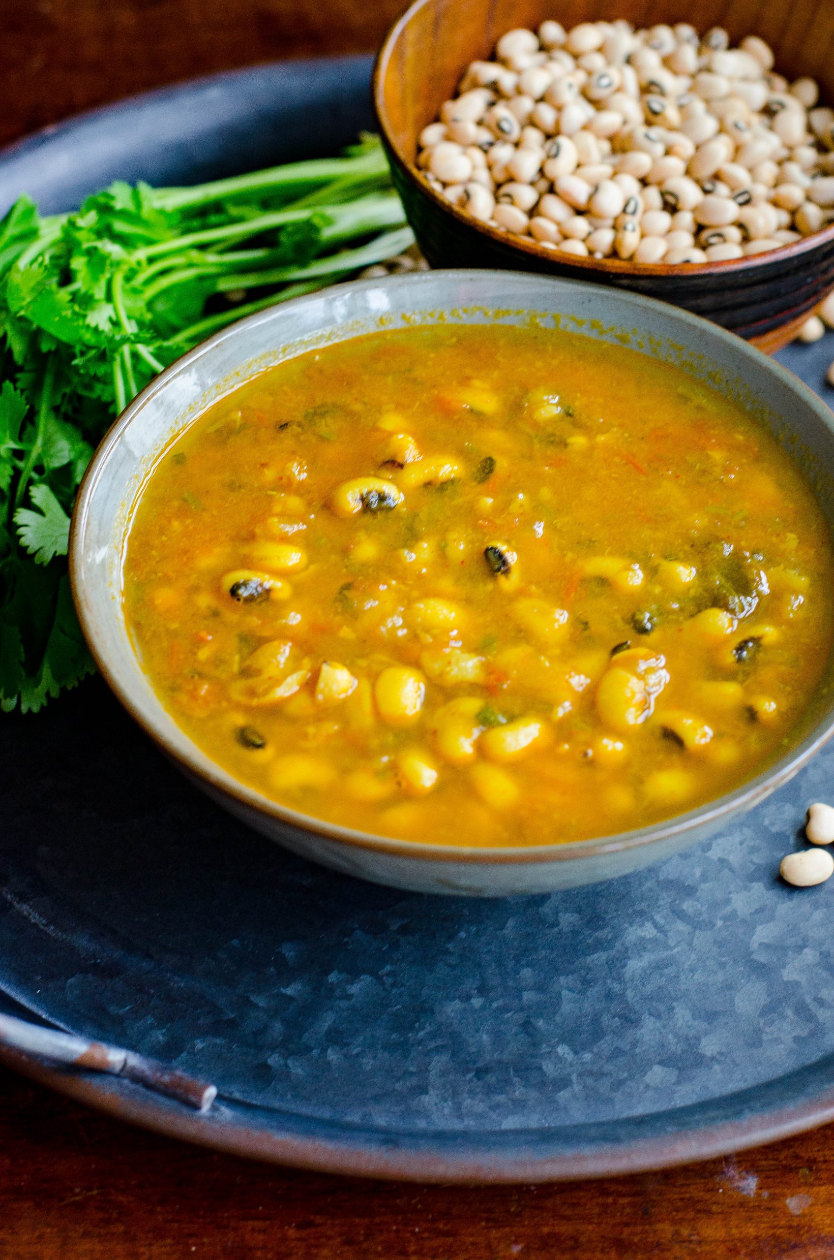 Black eyed peas curry served in a grey bowl placed on a blackish gray tray with scattered black eyed peas and cilantro at the background