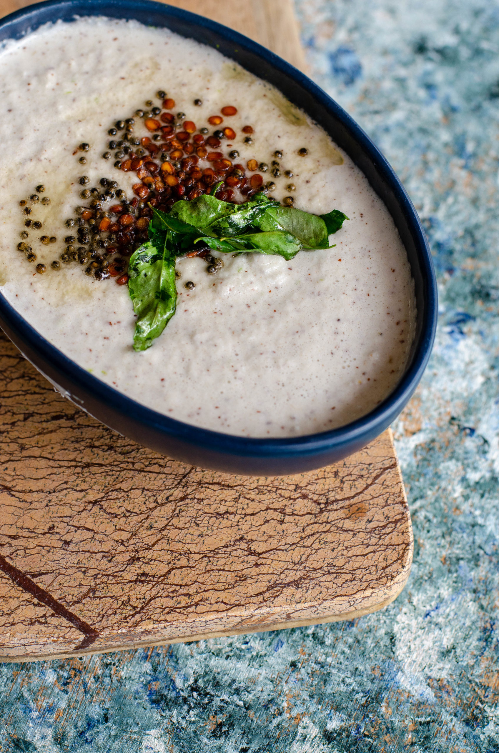 Salavai Chutney- South indian style vegan dip for Idli, dosa served in a blue bowl placed on a beige cheese board on a cement like backdrop.