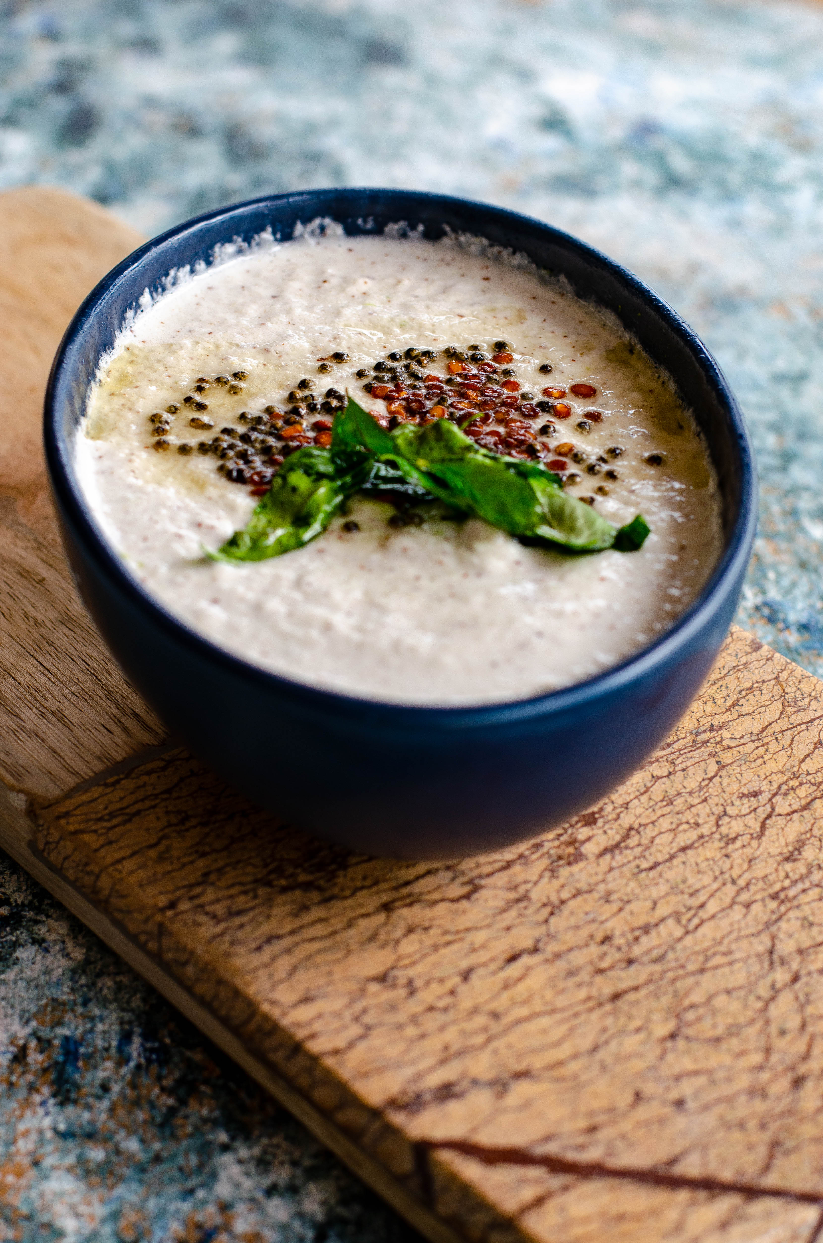 Salavai Chutney- South indian style vegan dip for Idli, dosa served in a blue bowl placed on a beige cheese board on a cement like backdrop.