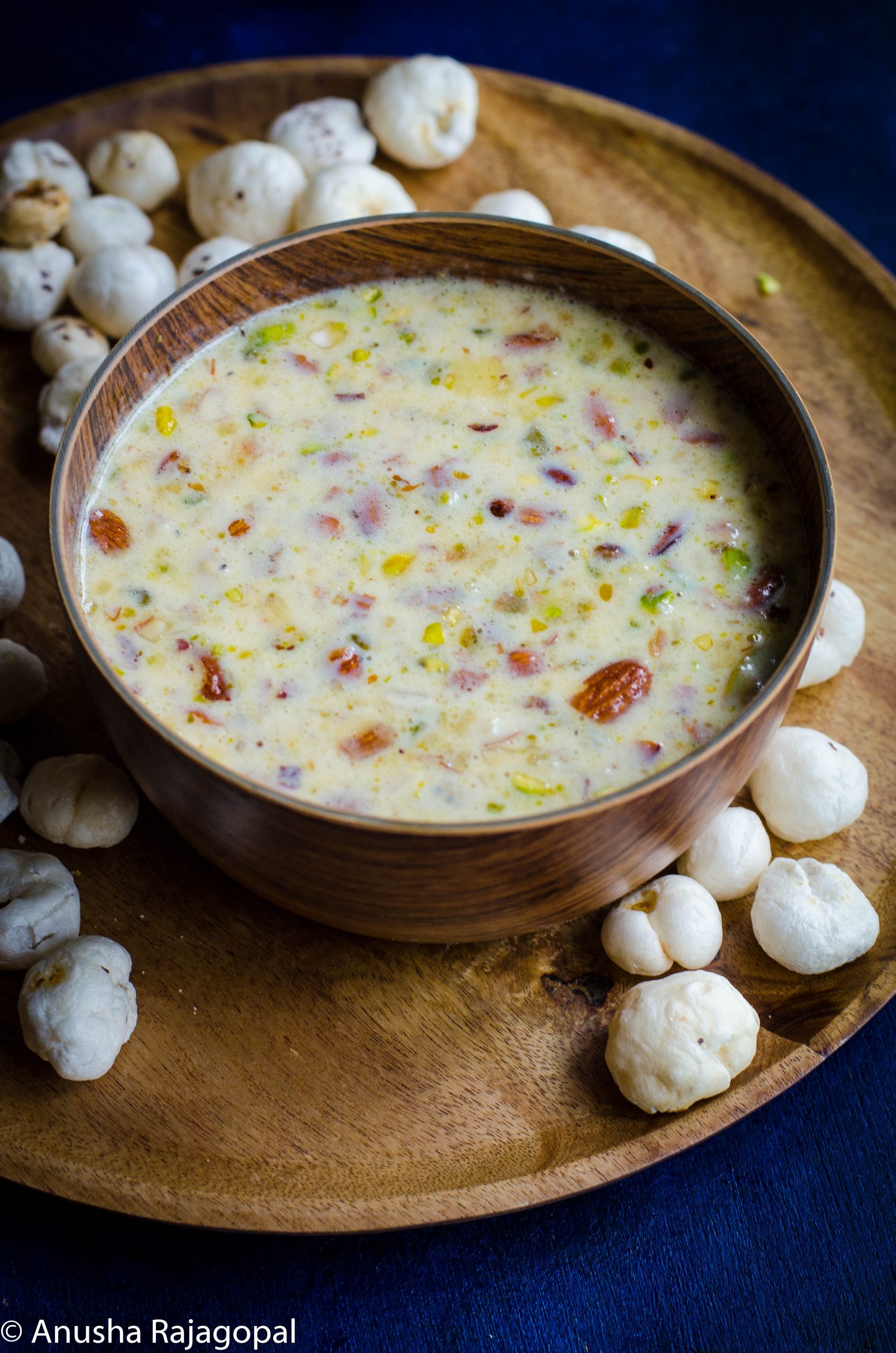Makhane Ki kheer served in a wooden bowl placed on a wooden plate with makhane in the background