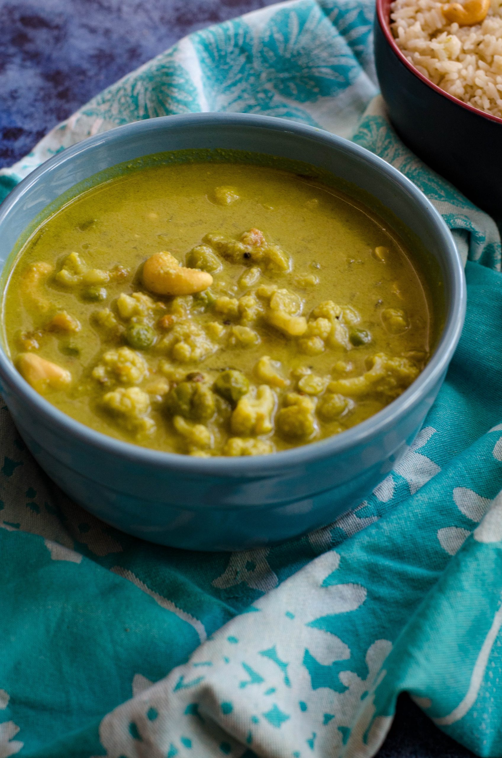 cauliflower cashew curry served in a blue bowl placed on a light blue napkin.