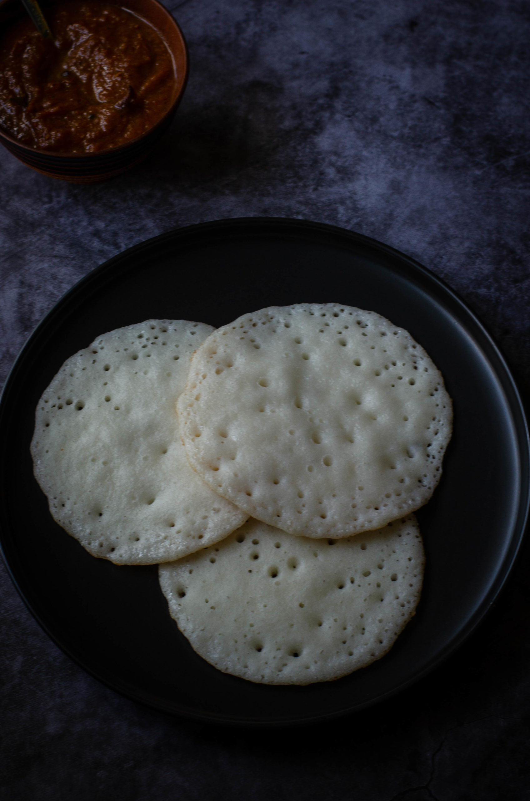 no ferment sponge dosa served on a black plate set against a grey backdrop