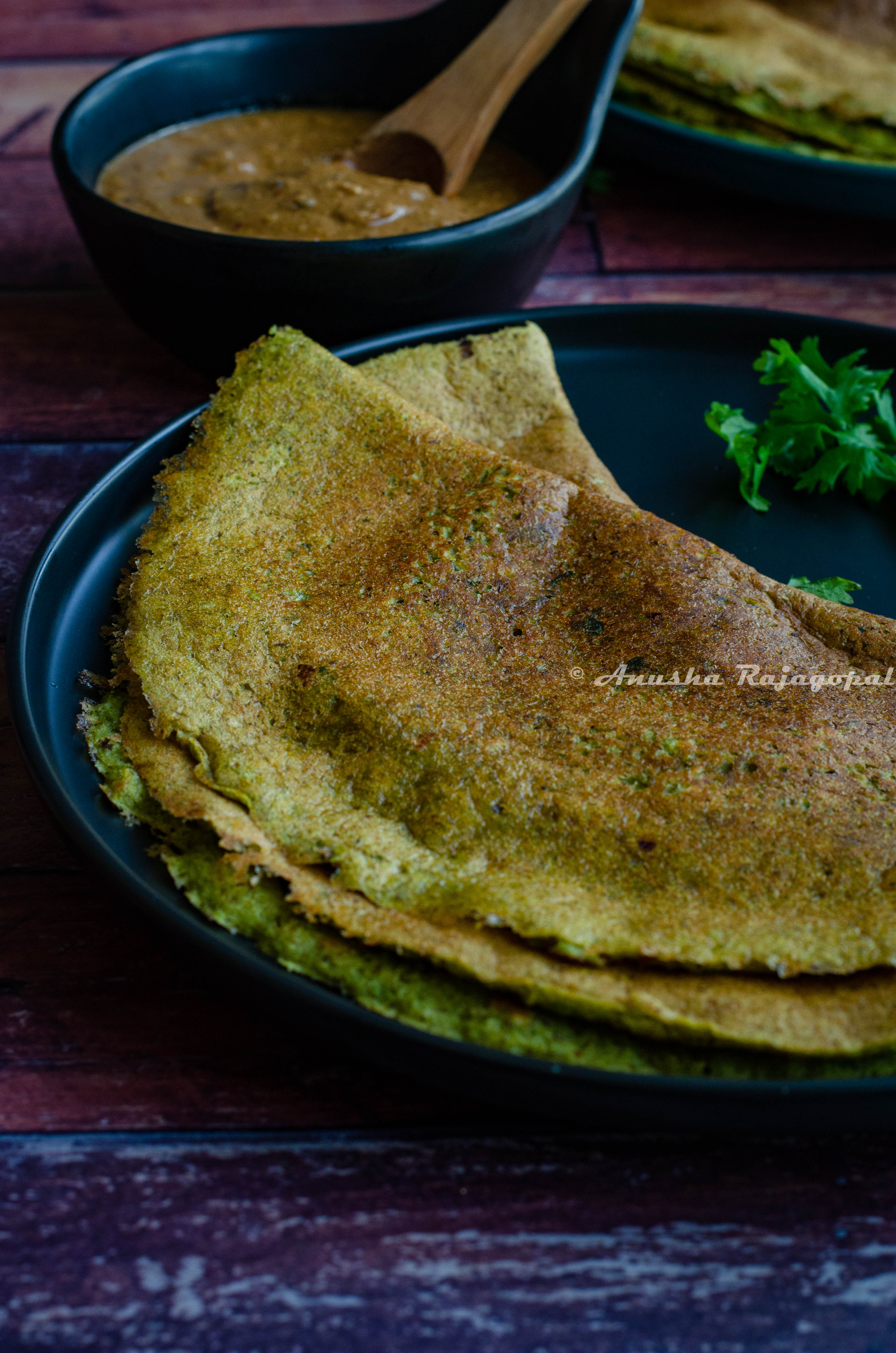 pesarattu- high protein moong beans dosa served on a black plate placed on a table.