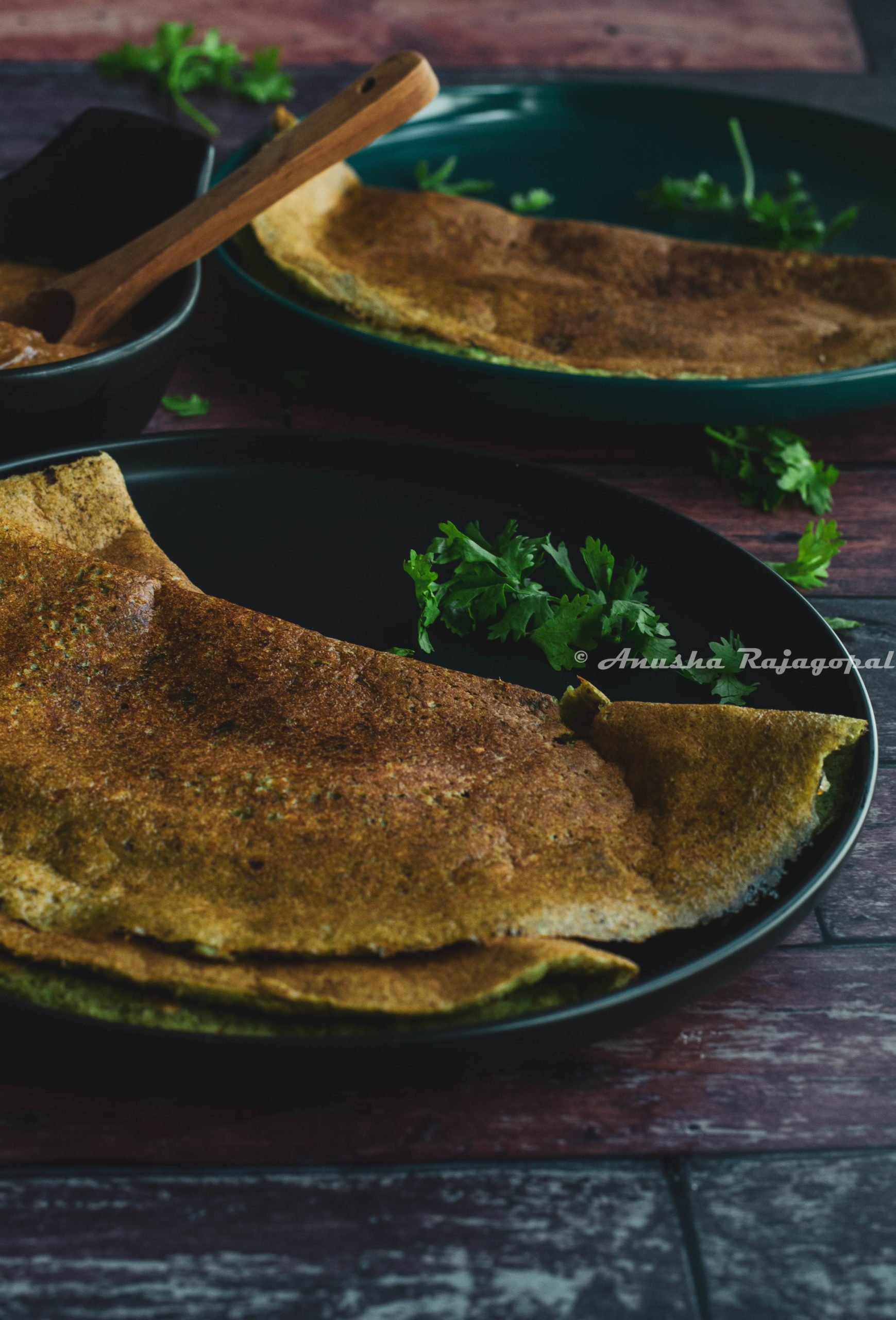 pesarattu- high protein moong beans dosa served on a black plate placed on a table.