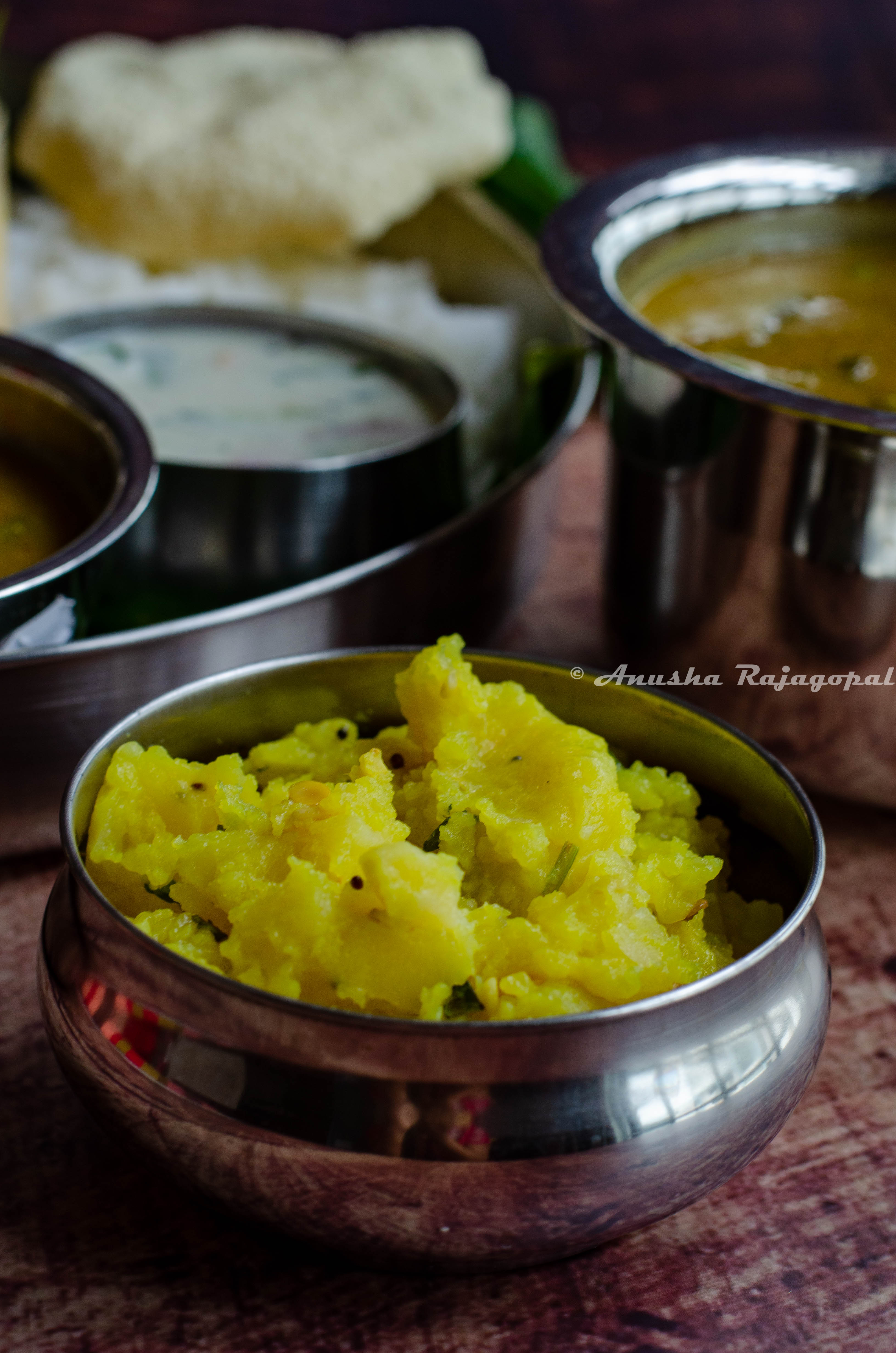 potato podimas served in a steel bowl with a full South Indian meal at the background