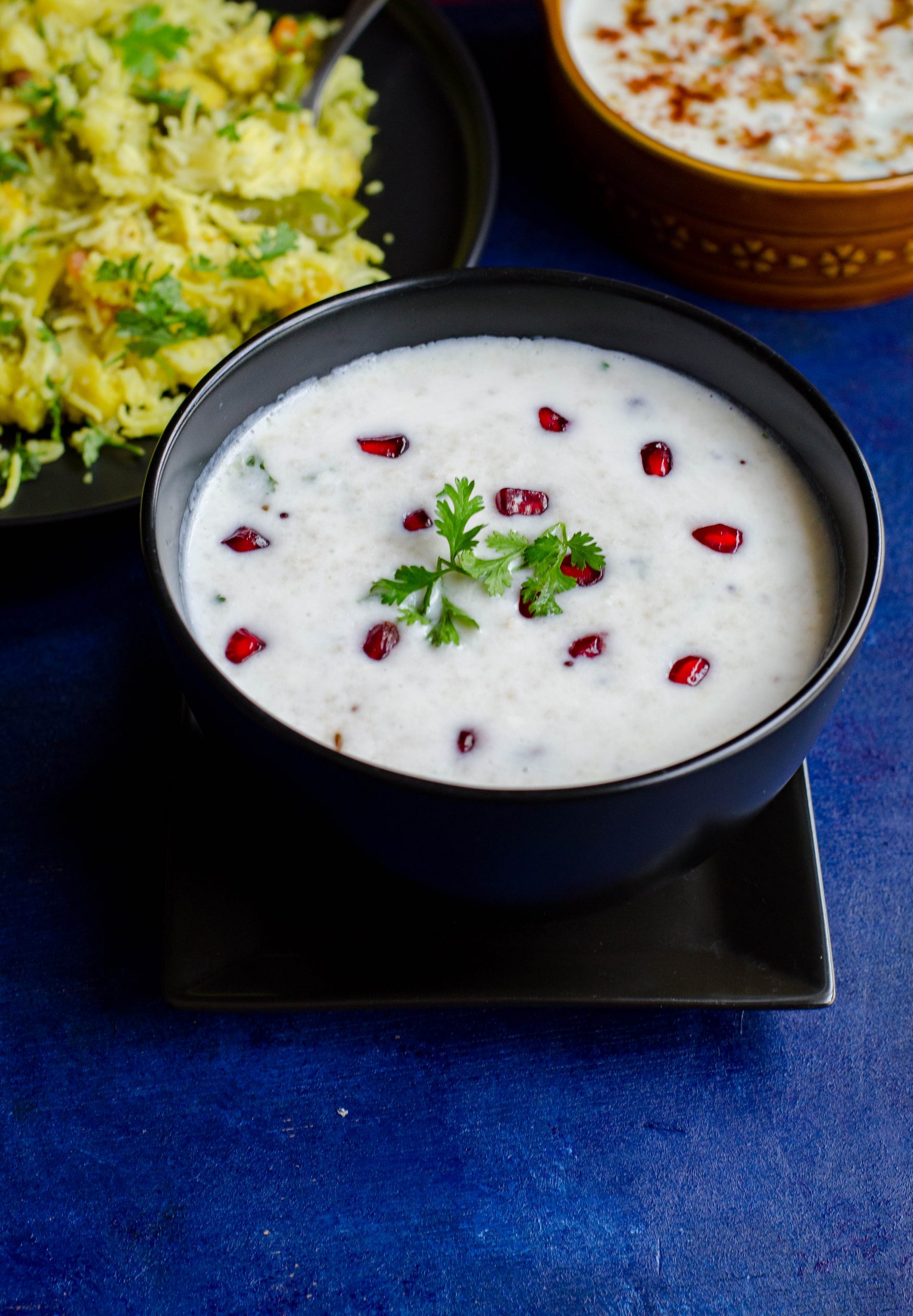 Samai Thayir Sadam served in a black bowl. Pomegranate pearls and cilantro as garnish.