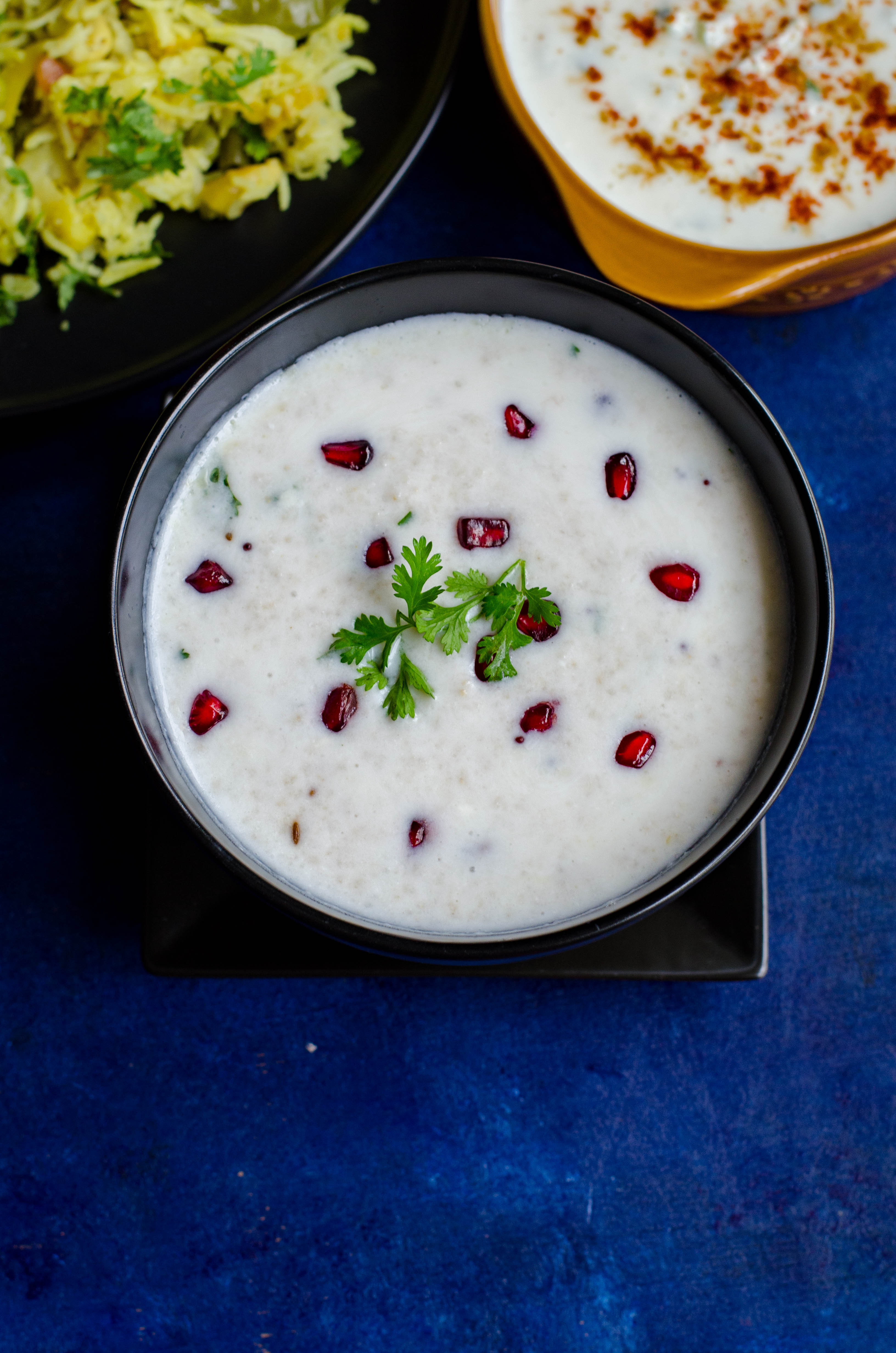 Little millet curd rice served in a black bowl set against a blue backdrop