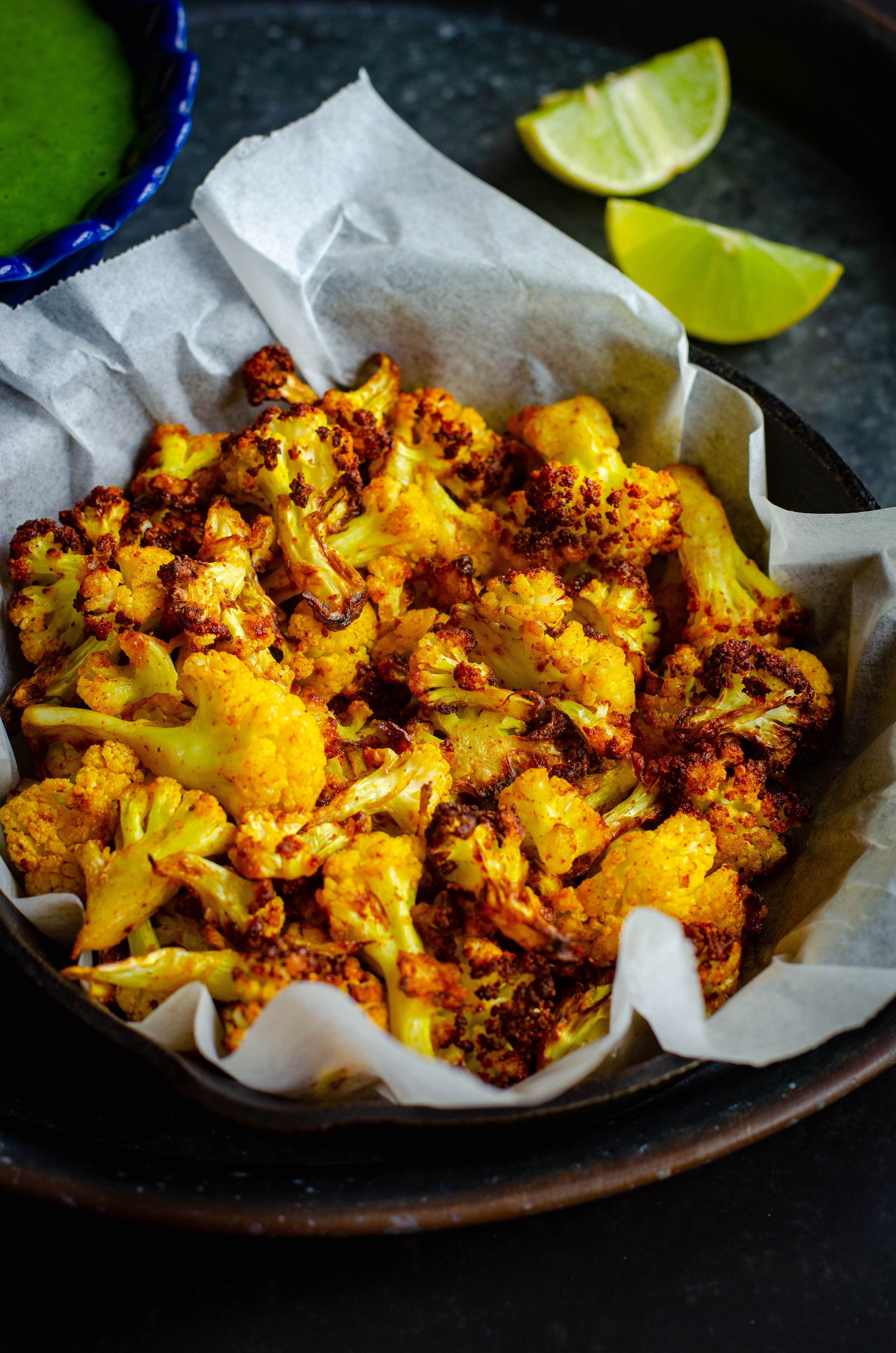 mexican air fryer caulilflower served in a tray with a mint dipping sauce and lemon wedges