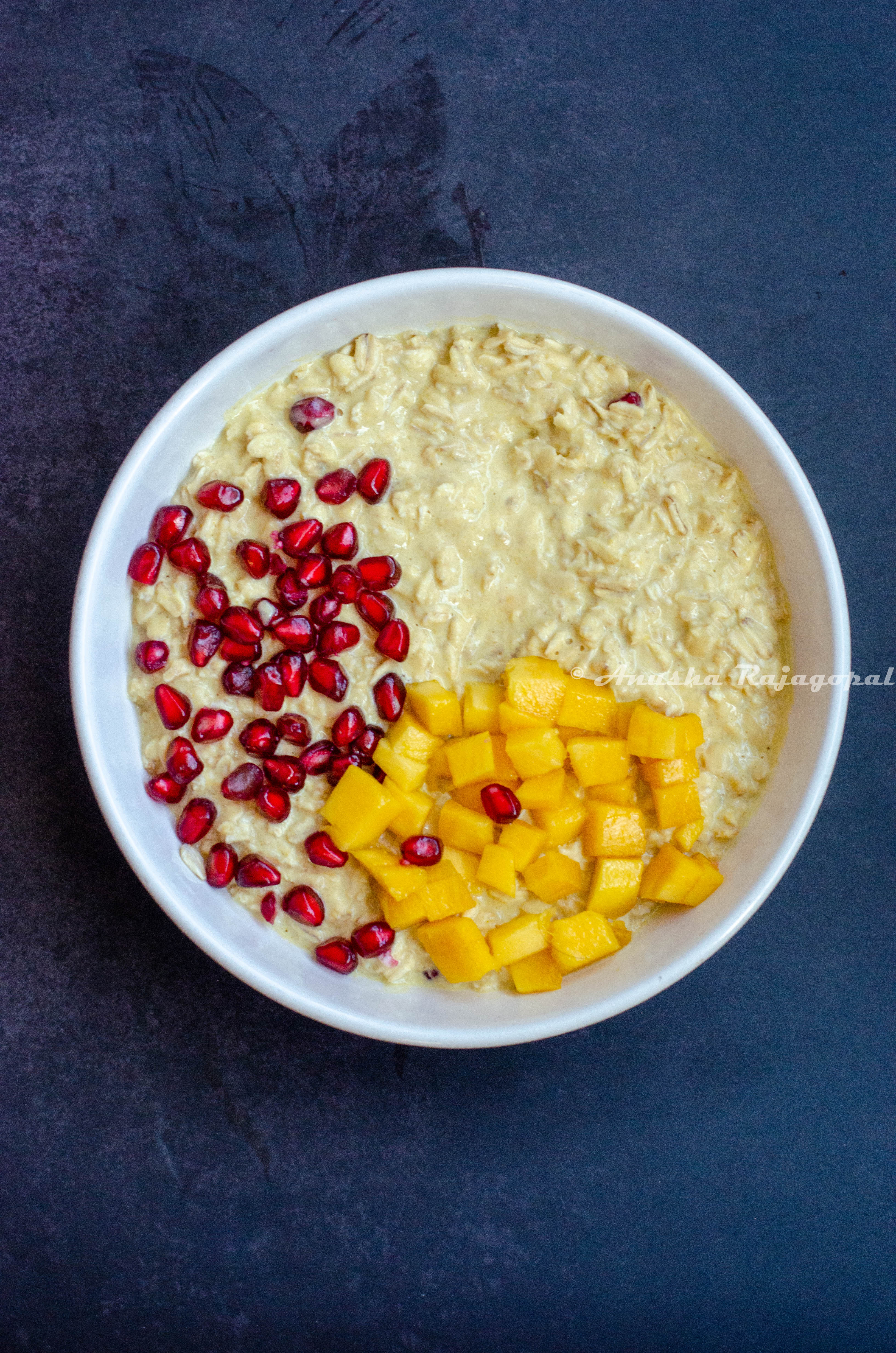 vegan mango overnight oats served in a white bowl topped with mangoes and pomegranate.